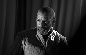 Denzel Washington as Macbeth looking contemplative in royal robe with curtained background (black and white photograph).