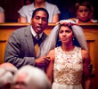 Emily in white wedding viel looks upset as father in three-piece suit has his hands on her shoulders comforting her with audience at the forefront and back of the image