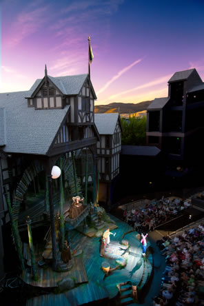 The timber-and-daub theater with a multilevel stage, the audience in an amphitheater, and sunset in the background