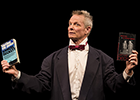 Bill Irwin, wearing a dinner  jacket, white shirt, and red bowtie, holds up in his right hand a well-read paper back edition of "Waiting for Godot" and in his left hand a paperback edition of "End Games" and "Acting Without Words."