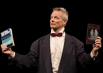 STC-On_Beckett-04_OB157_CraigSchwartz Bill Irwin, wearing a dinner jacket, white shirt, and red bowtie, holds up in his right hand a well-read paper back edition of "Waiting for Godot" and in his left hand a paperback edition of "End Games" and "Acting Without Words."